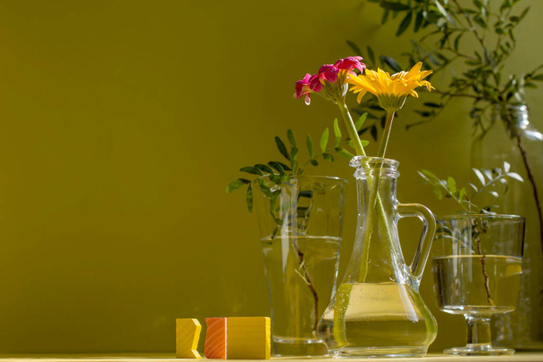 Piękne cienie szklanych wazonów w słońcu. Gerbery w szklanych butelkach na żółtym tle. Minimalistyczna koncepcja kwiatowa w nowoczesnym wnętrzu z surowym światłem i cieniem. Przestrzeń kopiowania. - Zdjęcie, obraz
