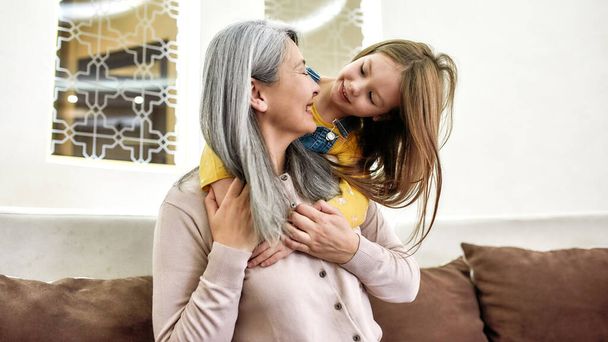 Special moments. Cute little child, granddaughter playing with her loving grandmother while spending time together at home - 写真・画像