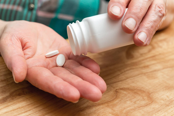 Bílé pilulky proti bolesti nebo antibiotika pro léčbu seniorské dlaně, léky a vitamínové doplňky koncept, detailní pohled. - Fotografie, Obrázek