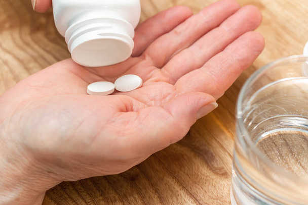 Pilules blanches d'analgésique ou d'antibiotique pour le traitement de la paume des mains de la femme âgée, verre avec de l'eau, médicaments et suppléments vitaminiques concept, vue rapprochée. - Photo, image