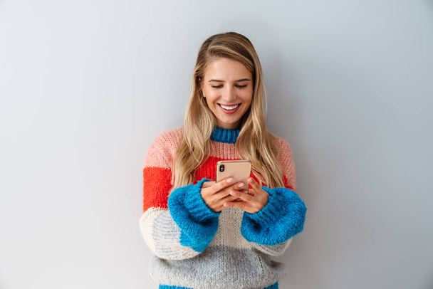 Smiling young woman using smartphone over gray background - Fotó, kép