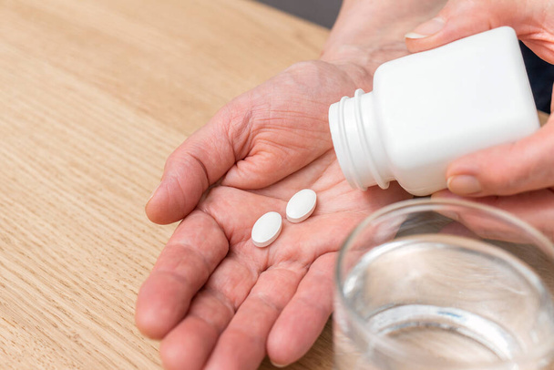 Білі таблетки знеболюючого засобу або антибіотика для лікування на руці старшої жінки, скло з водою, ліки та концепція вітамінних добавок, крупним планом
. - Фото, зображення