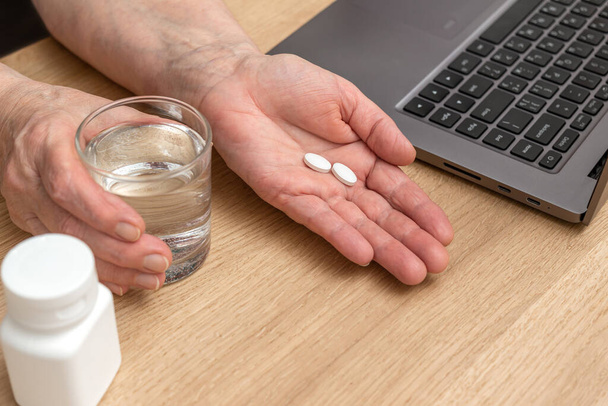 高齢女性の手掌の治療のための鎮痛剤または抗生物質の白い丸薬,水とガラス,薬やビタミンサプリメントの概念,クローズアップビュー. - 写真・画像