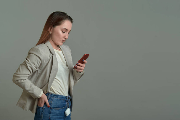cute girl with a phone in her hands on a gray background - Foto, Imagen