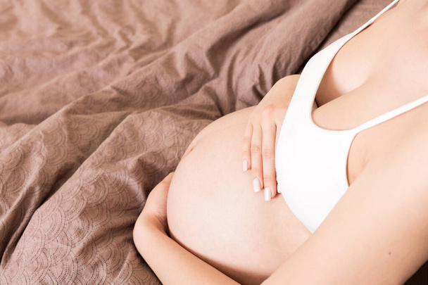zwangere vrouw die thuis haar buik aanraakt. zwangerschapsverwachting concept. - Foto, afbeelding