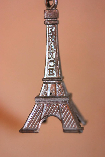 Metalowy breloczek w formie wieży Eiffla w Paryżu, Francja. Pamiątka z podróży zbliżenie na pomarańczowym tle - Zdjęcie, obraz