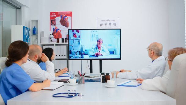 病院の会議室の机に座ってビデオ会議を持っている医師のチーム - 写真・画像