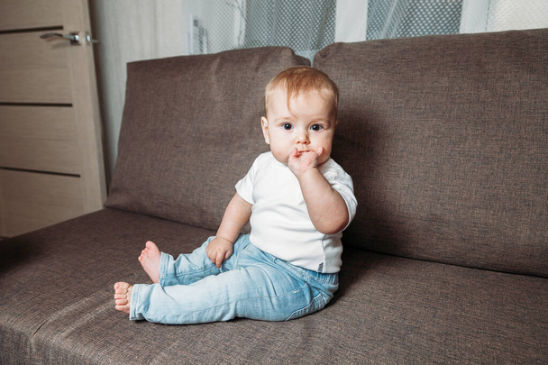 adorable bébé fille assis sur le canapé avec les doigts dans la bouche - Photo, image