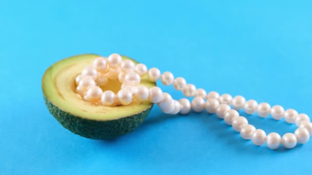Half fresh avocado fruit with pearls on blue background. Fashionable food design. - Footage, Video
