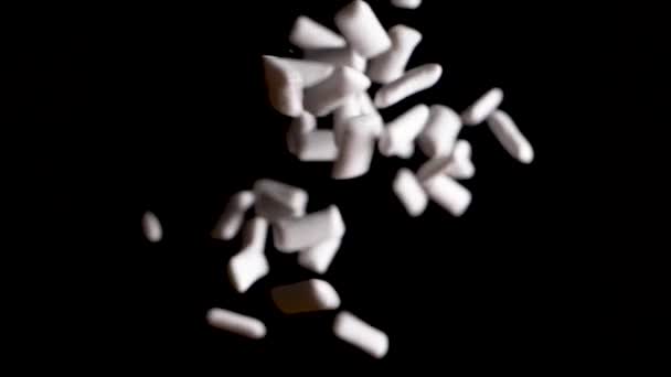 Bílé žvýkačky padající shora do černého pozadí ve zpomaleném filmu - Záběry, video