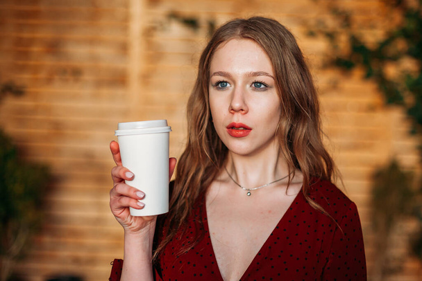 young beautiful woman in a cafe with a white paper Cup of coffee in her hands - Foto, Bild