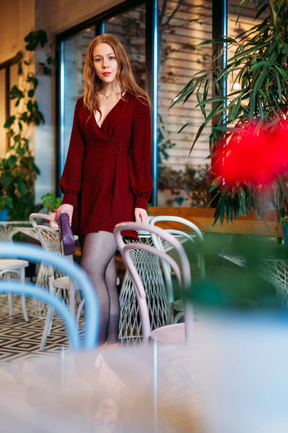 bella donna bionda è in piedi in un caffè tra tavoli e sedie. - Foto, immagini