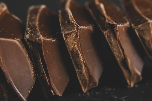 Broken dark chocolate blocks stack on black background - Фото, изображение