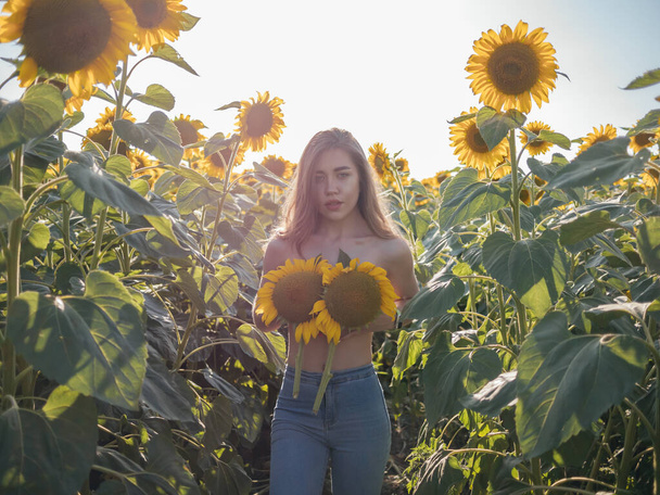 Funny photo of beautiful woman with long hair smiling and holding yellow sunflower at sunset. Fun fermer. Summer concept. - Foto, imagen