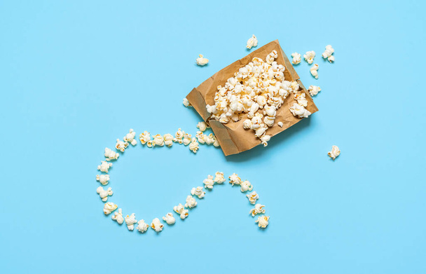 Popcorn exploding in paper bag with fuse, isolated on blue background. Flat lay with popcorn bag, homemade. Microwave pop-corn bag. Movie time concept - Photo, Image