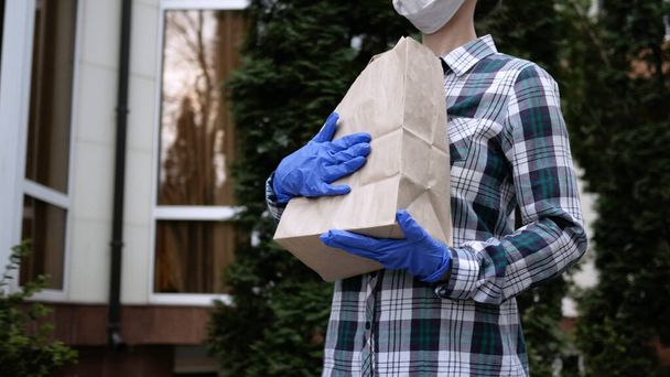 Courier, delivery man in protective mask and medical gloves delivers takeaway food. Delivery service under quarantine, disease outbreak, coronavirus covid-19 pandemic conditions. Stay home. - Valokuva, kuva