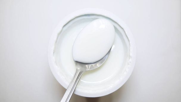 widok z góry słoika z jogurtem izolowane na białym tle. Jedz łyżkę jogurtu z bliska. - Zdjęcie, obraz