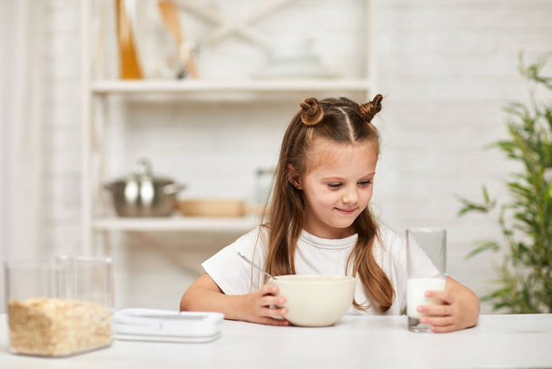 little girl eating breakfast: cereal with the milk in the kitchen. - Foto, imagen