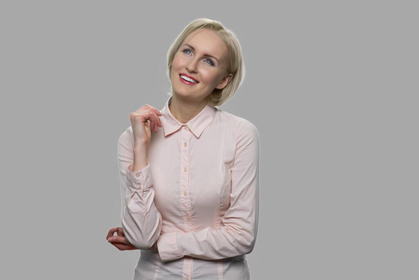 Smiling business woman daydreaming on gray background. - Zdjęcie, obraz
