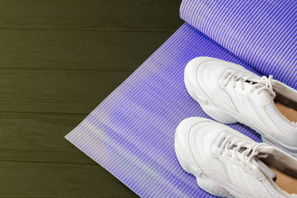 коврик для йоги и спортивная обувь на черном фоне. Здоровый образ жизни, йога, концепция s.ports - Фото, изображение