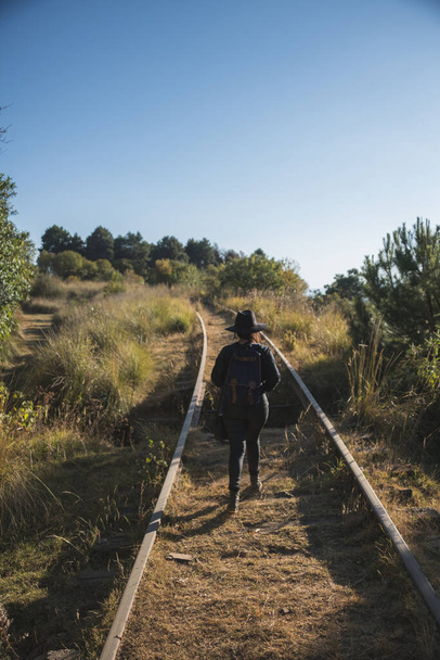 Retrato de uma menina aventureira, explorando novas trilhas, vestida de preto, com uma mochila azul, chapéu e uma mochila preta. 2 - Foto, Imagem