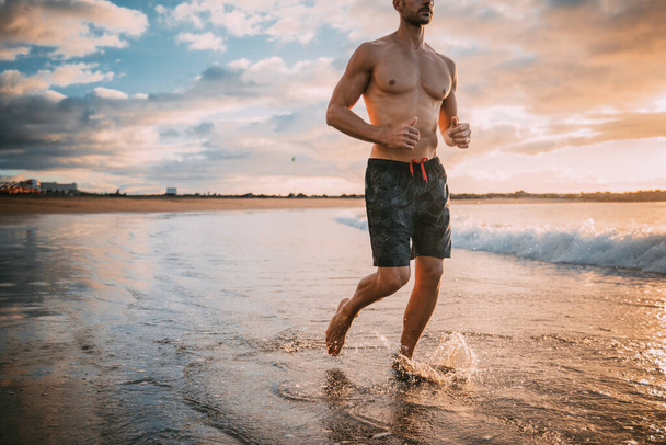 Genç bir adam plajda gün batımında egzersiz yapıyor. Sıcak renkler - Fotoğraf, Görsel