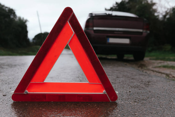 κόκκινο προειδοποιητικό τρίγωνο στο δρόμο μπροστά από ένα σπασμένο αυτοκίνητο - Φωτογραφία, εικόνα