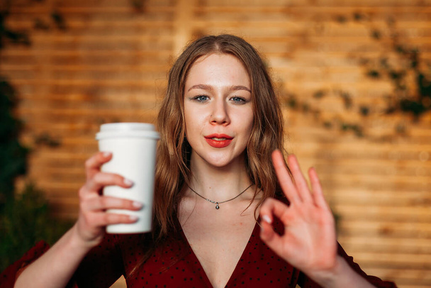 Frau mit einer Tasse heißen Kaffees in der Hand. Frau zeigt ok Geste. Coffeeshop-Werbung. Platz für die eigene Familie - Foto, Bild