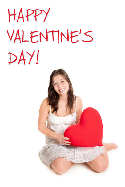 Schönes Mädchen mit rotem Herzkissen, Text glücklich Valentinstag in der oberen linken Ecke, isoliert vor weißem Studiohintergrund - Foto, Bild