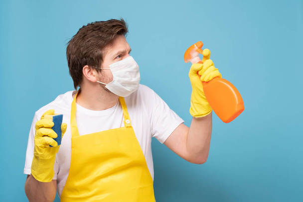 Молодой человек в фартуке, защитная маска и перчатки готовы очистить все от коронавируса. - Фото, изображение