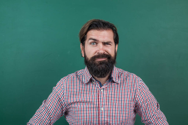 express human emotions. caucasian hipster with beard on green background. confused mature teacher on background of blackboard. brutal bearded man wear casual checkered shirt. he is so handsome - Zdjęcie, obraz
