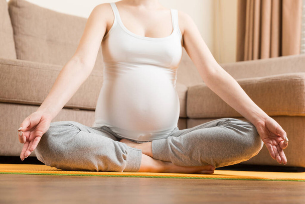 Беременная женщина медитирует, сидя в положении йоги. Медитация на тему материнства Беременность Йога и фитнес концепция в коронавирусное время. - Фото, изображение