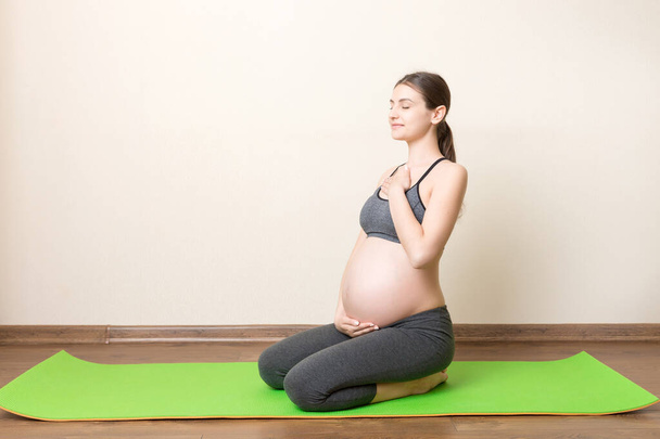 Schöne schwangere Frau beim Yoga zu Hause. Schwangerschaft Yoga und Fitness-Konzept zur Zeit des Coronavirus. - Foto, Bild