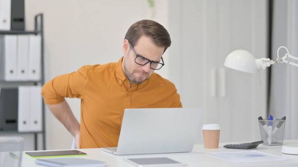 Giovane uomo con computer portatile con mal di schiena in ufficio  - Foto, immagini