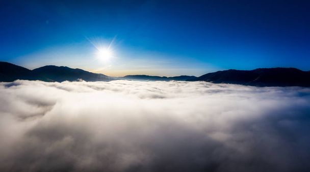 Sunrise over mountain hils covered with gray mist. Aerial panoramic drone shot - 写真・画像