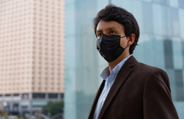 Giovane uomo latino che indossa una maschera facciale per motivi protettivi durante la pandemia covid 19 - Foto, immagini