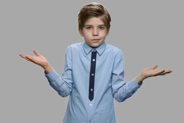 Boy shrugging shoulders against gray background. - Photo, Image