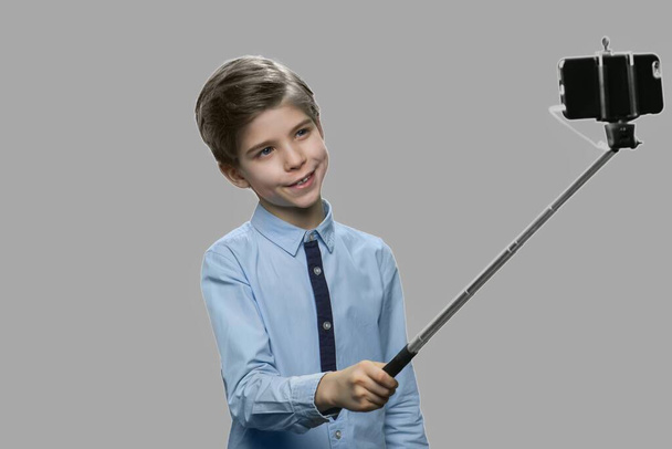 Αστείο αγόρι που χρησιμοποιεί monopod σε γκρι φόντο. - Φωτογραφία, εικόνα