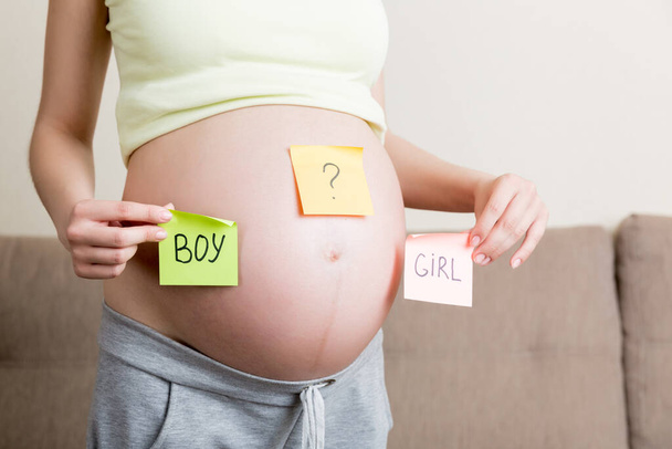 έγκυος γυναίκα που κρατά τετράγωνα πολύχρωμα αυτοκόλλητα με ερωτηματικά. - Φωτογραφία, εικόνα