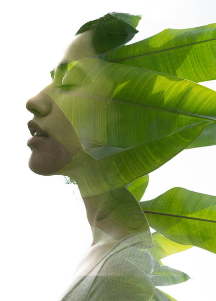 A double exposure portrait young woman profile with her eyes closed against white background and tropical foliage - Valokuva, kuva