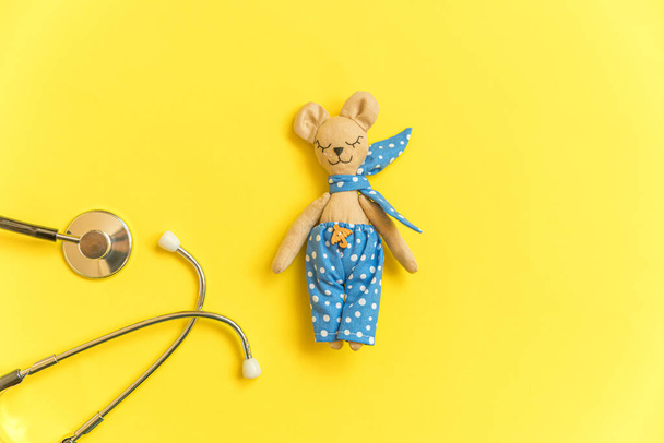 Просто минимальный дизайн игрушки медведя и медицинского оборудования стетоскоп изолирован на желтом фоне. Здравоохранение детский врач концепция. Символ педиатра. Плоское пространство для копирования с видом сверху - Фото, изображение