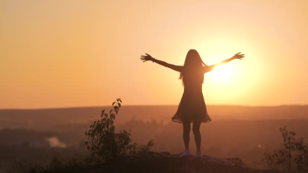 Silhouette sombre d'une jeune femme debout les mains levées sur une pierre profitant d'une vue coucher de soleil à l'extérieur en été. - Séquence, vidéo