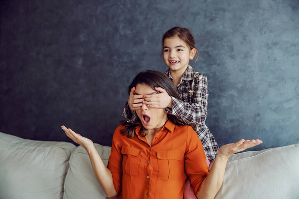 Smiling child covering her mother's eyes and smiling. Mother is surprised. Mother and daughter playing games concept. - Photo, Image