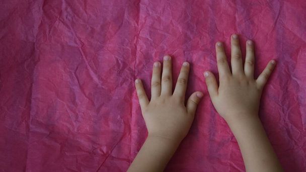 Widok z góry dłoni dziecka dotknąć różowy pognieciony papier na stole z miejsca do kopiowania - Zdjęcie, obraz