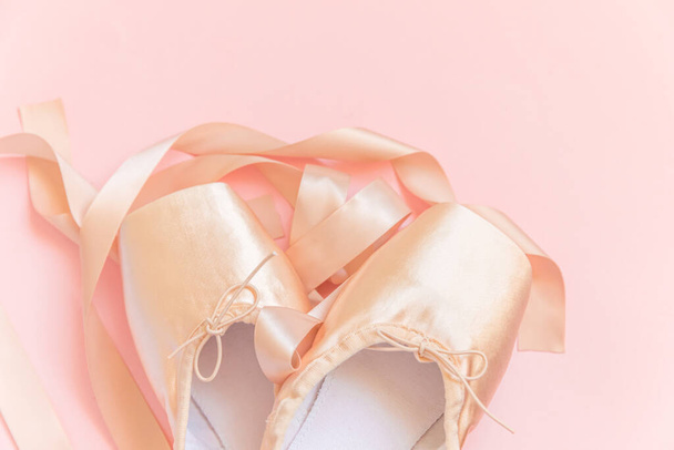 Нові туфлі для бежевого балету з атласною стрічкою, ізольованими на рожевому тлі. "Балерина" - класичне взуття для тренування танців. Концепція балетної школи. Top view flat lay copy space - Фото, зображення