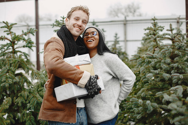 Mixed couple standing with gifts by the Christmas tree - Photo, image