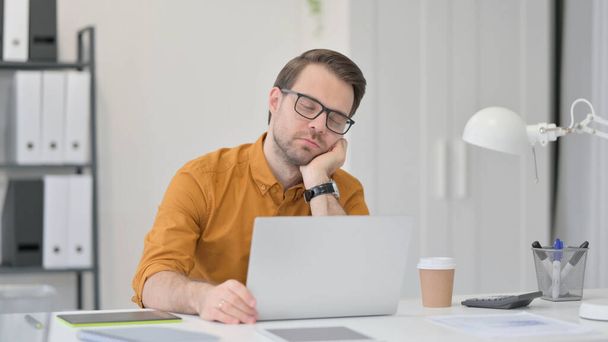 Jeune homme avec ordinateur portable faisant la sieste au bureau  - Photo, image