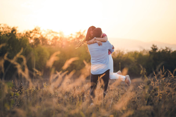 Outdoor portrait of young couple, boyfriend lifts his girlfriend in air. Afternoon light. Romance, romantic gestures - Photo, Image
