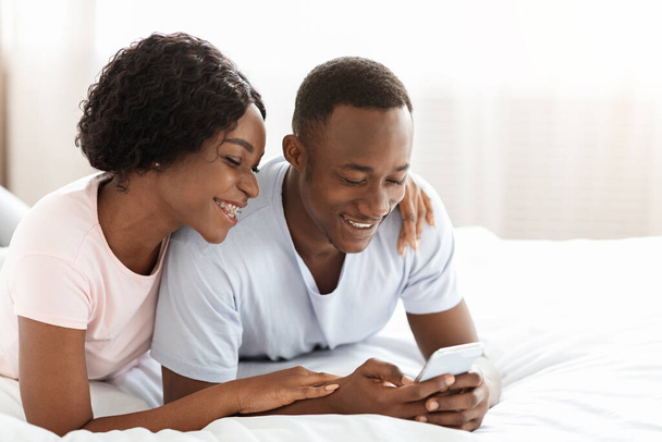Vreugdevol Afrikaans Amerikaans paar met behulp van app samen op smartphone - Foto, afbeelding