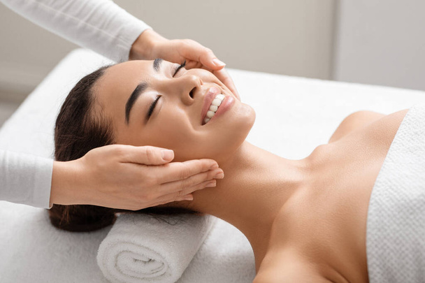 Young Smiling Korean Woman Enjoying Spa Facial Massage In Beauty Salon - Photo, Image